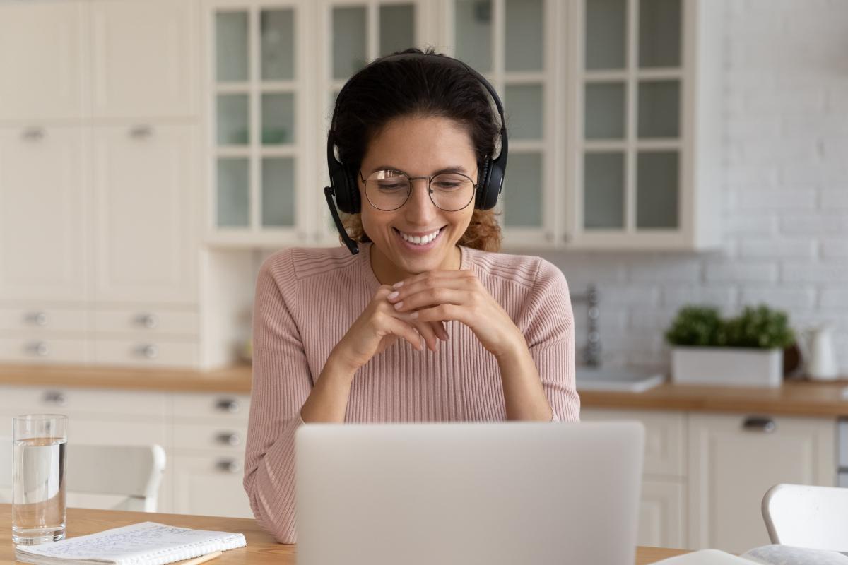 Una persona è seduta davanti al suo computer portatile, collegata da remoto per fornire assistenza clienti e consulenza d'acquisto. E' visibilmente felice, grazie alla flessibilità con cui può svolgere il suo lavoro, e per la facilità di Zoom Contact Center. 